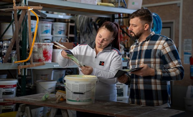 Eine Malerin und ein Maler schauen sich zusammen eine Farbpalette in ihrem Betrieb an.