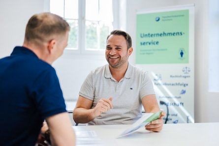 Mitarbeiter der Handwerkskammer berät einen Kunden an einem Tisch.