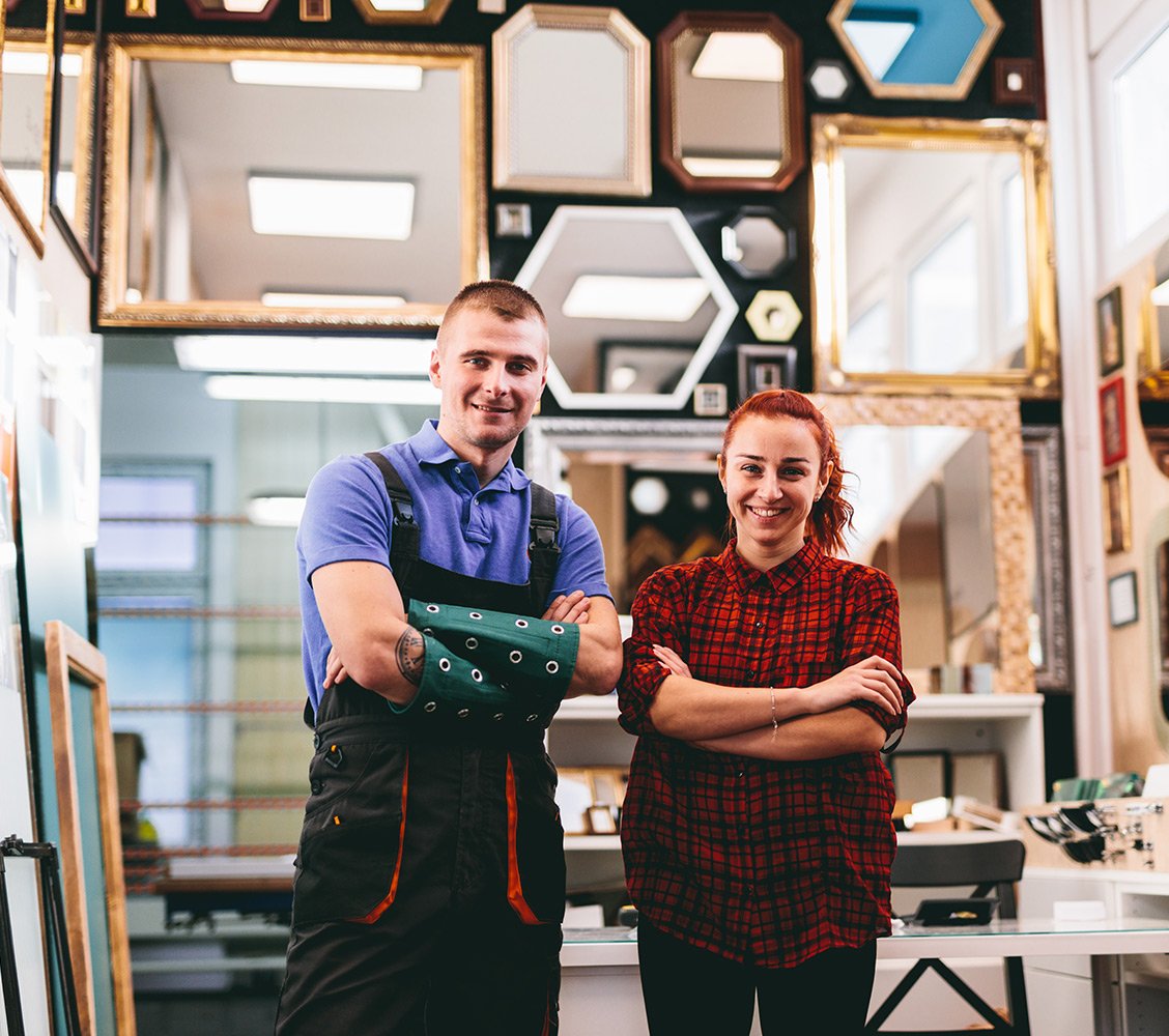 Eine Handwerkerin und ein Handwerker stehen in ihrem Betrieb.
