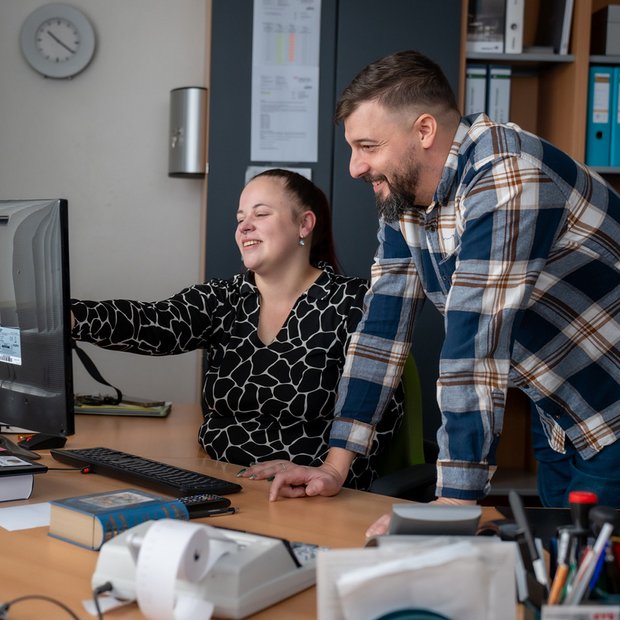 Zwei Mitarbeiter besprechen Inhalte auf einem Computer im Büro.