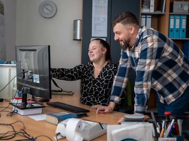 Zwei Mitarbeiter besprechen Inhalte auf einem Computer im Büro.